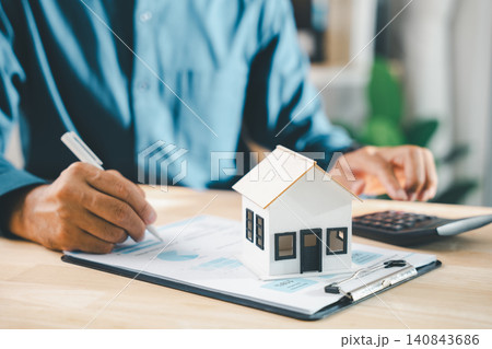 Real estate contract property mortgage finance signing approved, client signs home buying insurance document near homeowner tenant investment papers, calculator and house model on desk 140843686