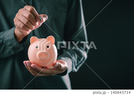 Personal savings financial planning concept with man holding pink piggy bank for retirement investment and wealth growth, putting silver coin inside for future security 140843714