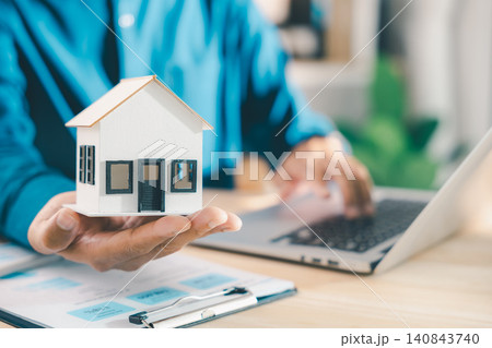 Real estate contract property mortgage finance approved insurance home document for homeowner tenant investment shows hand holding house model while using laptop computer at office desk 140843740