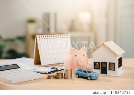 Real estate investment growth management and property asset invest features house model near pink piggy bank, while blue car sits beside rising coins with desk calendar and calculator Real estate investment growth management and property asset invest features house model near pink piggy bank, while blue car sits beside rising coins with desk calendar and calculator 140843752