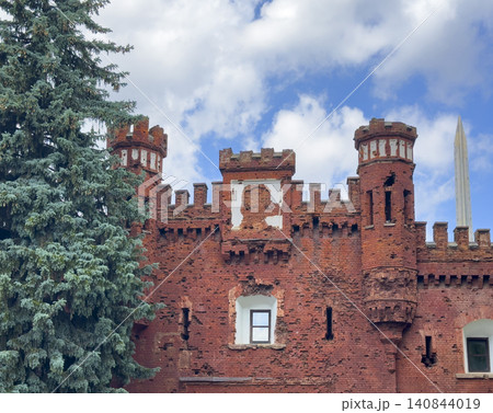 Red brick fortress tower rises near trees against sky. Historic architecture stands tall with strong walls and details. Cultural landmark concept reflects history, heritage, travel Red brick fortress tower rises near trees against sky. Historic architecture stands tall with strong walls and details. Cultural landmark concept reflects history, heritage, travel 140844019