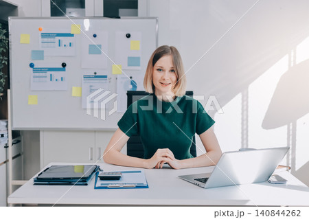 Concept of business working, Businesswoman sitting while writing and checking business analytic document report and holding tablet with computer pc, smartphone on desk in her workstation. Concept of business working, Businesswoman sitting while writing and checking business analytic document report and holding tablet with computer pc, smartphone on desk in her workstation. 140844262