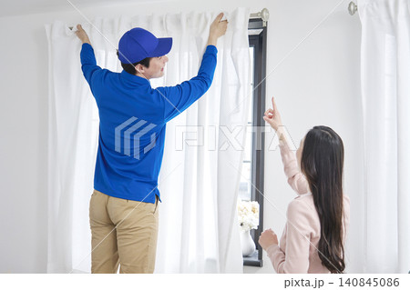 引っ越し業者がカーテンを取り付け女性が指示する 140845086