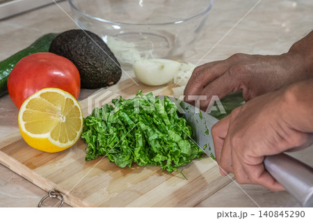 Man is chopping fresh green vegetables on a wooden cutting board. Cropped view of close up male hands cutting organic vegetables for salad. Healthy eating habits. Food preparation concept Man is chopping fresh green vegetables on a wooden cutting board. Cropped view of close up male hands cutting organic vegetables for salad. Healthy eating habits. Food preparation concept 140845290