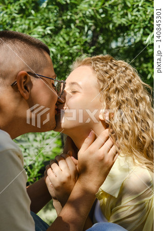 Couple sharing kiss in natural setting with greenery around them during warm afternoon Couple sharing kiss in natural setting with greenery around them during warm afternoon 140845301