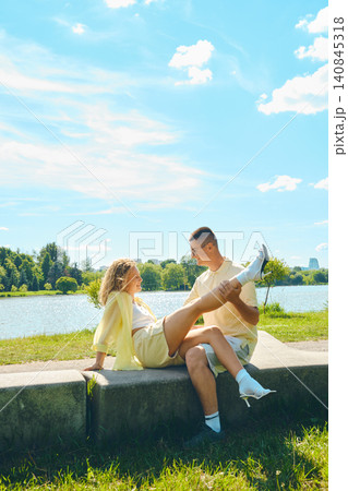 Couple enjoys sunny day by river while sitting on stone ledge in park Couple enjoys sunny day by river while sitting on stone ledge in park 140845318