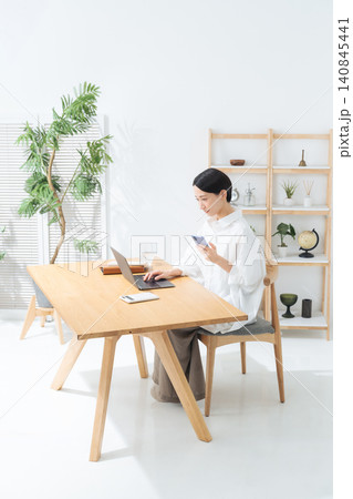 部屋でスマホとノートパソコンを使う女性。アプリ、フリーランス、仕事、ライフスタイル、DX 140845441