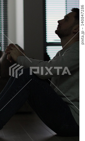 Vertical video Silhouette of a sad man sitting in the dark leaning against the wall in home. Family problems, stress. Vertical video Silhouette of a sad man sitting in the dark leaning against the wall in home. Family problems, stress. 140847286