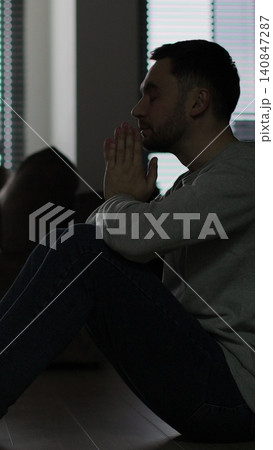 Vertical video Silhouette of a sad man sitting in the dark leaning against the wall in home. Family problems, stress. Vertical video Silhouette of a sad man sitting in the dark leaning against the wall in home. Family problems, stress. 140847287