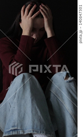 Vertical video Sad woman sitting in the dark leaning against the wall in home. Domestic violence, family problems, stress, violence. Vertical video Sad woman sitting in the dark leaning against the wall in home. Domestic violence, family problems, stress, violence. 140847301