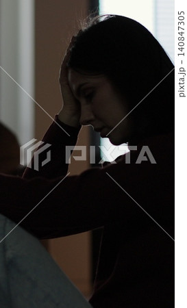 Vertical video Silhouette of a sad woman sitting in the dark leaning against the wall in home. Domestic violence, family problems, stress, violence. Vertical video Silhouette of a sad woman sitting in the dark leaning against the wall in home. Domestic violence, family problems, stress, violence. 140847305