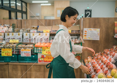 スーパーマーケットの果物売り場で横向きに微笑みながら陳列する女性店員 スーパーマーケットの果物売り場で横向きに微笑みながら陳列する女性店員 140848616