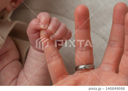 A heartwarming conceptual photo showing the size difference between a parent's hand with a wedding ring and a newborn baby's tiny fist. Concept of fatherhood, safety, and family growth. Macro 140849098