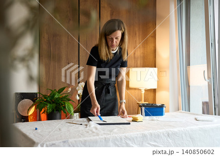 Woman artist creating textured picture on canvas at home 140850602