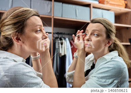 Woman plucking eyebrows in wardrobe mirror 140850621