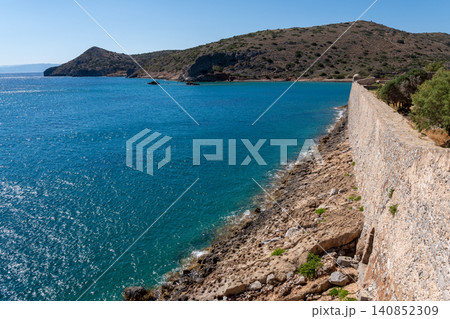 Long historic stone fortress wall by blue sea on Spinalonga island Greece Long historic stone fortress wall by blue sea on Spinalonga island Greece 140852309