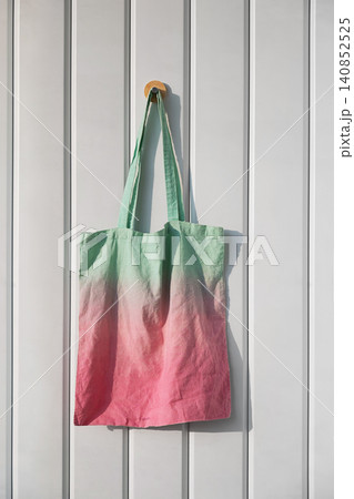Tote bag with green and pink gradient hanging on wall. Reusable cloth accessory for shopping Tote bag with green and pink gradient hanging on wall. Reusable cloth accessory for shopping 140852525