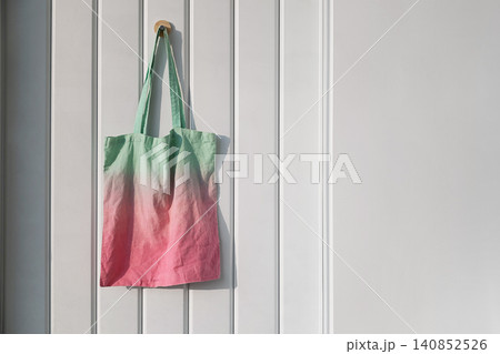 Green and pink gradient cotton tote bag hanging on wooden door. Eco friendly reusable shopper Green and pink gradient cotton tote bag hanging on wooden door. Eco friendly reusable shopper 140852526