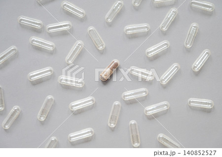 One filled medicine capsule surrounded by empty clear pills on gray background. One filled medicine capsule surrounded by empty clear pills on gray background. 140852527