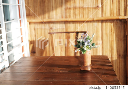 Plastic flowers in a bamboo vase decorate a wooden table in natural sunlight at the resort in Thailand. Copy space 140853545
