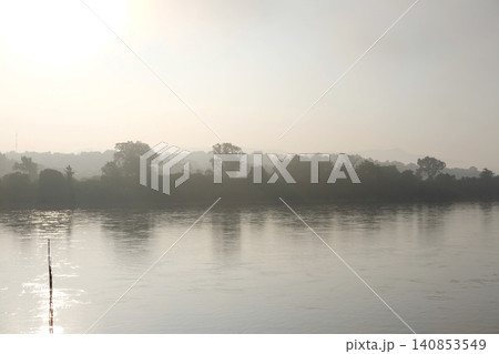 Beautiful golden sunrise illuminates in the morning with mist and the river is peaceful and ethereal scene in nature of Thailand Beautiful golden sunrise illuminates in the morning with mist and the river is peaceful and ethereal scene in nature of Thailand 140853549