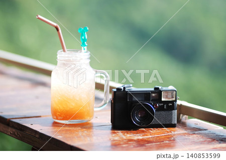 Fresh plum juice and vintage analog film camera on wooden bar on terrace in resort on the mountain in Thailand Fresh plum juice and vintage analog film camera on wooden bar on terrace in resort on the mountain in Thailand 140853599