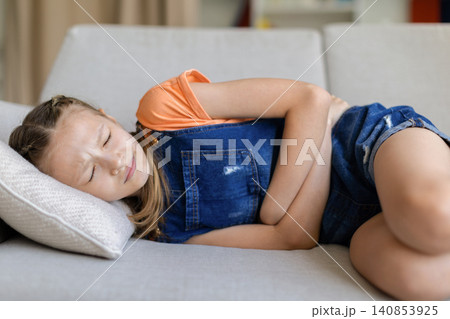 Teen girl lying on sofa at home holding stomach with eyes closed Teen girl lying on sofa at home holding stomach with eyes closed 140853925