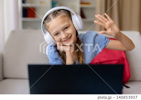 Happy teen girl in headphones waving at laptop camera during virtual class 140853937