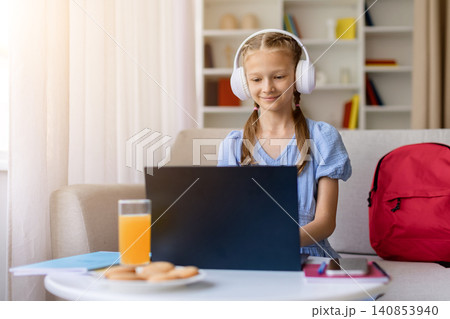 Teen girl wearing white headphones studies on laptop at home Teen girl wearing white headphones studies on laptop at home 140853940