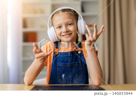 Smiling teen girl wearing white headphones gesturing during online lesson at home Smiling teen girl wearing white headphones gesturing during online lesson at home 140853944