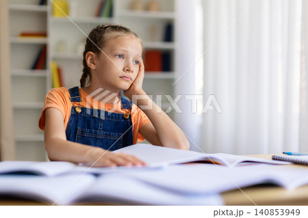 Bored teen girl looking away, sitting at table with books at home Bored teen girl looking away, sitting at table with books at home 140853949