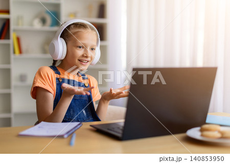 Teen girl wearing headphones gesturing while speaking to laptop at home Teen girl wearing headphones gesturing while speaking to laptop at home 140853950