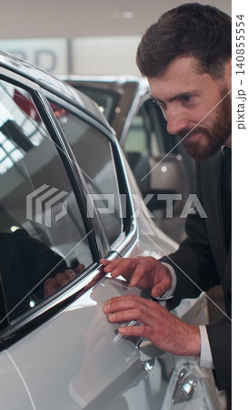 Vertical Video Stylish man is choosing new automobile walking around luxury car and touching it in car dealership. Rich people, transportation and business class vehicles concept. 140855554