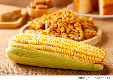 Boiled corn on the cob on a table featuring traditional Brazilian foods, with homemade pe de moleque in the background. Boiled corn on the cob on a table featuring traditional Brazilian foods, with homemade pe de moleque in the background. 140855713