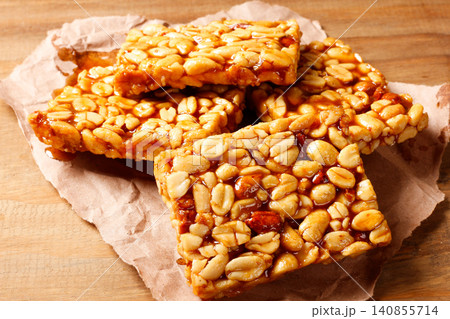 Traditional Brazilian pe de moleque made with caramelized peanuts and a glossy syrup, arranged on rustic paper atop a wooden table Traditional Brazilian pe de moleque made with caramelized peanuts and a glossy syrup, arranged on rustic paper atop a wooden table 140855714