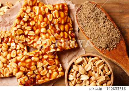 Traditional Brazilian pe de moleque made with caramelized peanuts, accompanied by roasted peanuts and brown sugar on a rustic wooden surface Traditional Brazilian pe de moleque made with caramelized peanuts, accompanied by roasted peanuts and brown sugar on a rustic wooden surface 140855718
