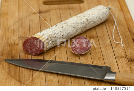 Slicing gourmet sausage on a wooden cutting board in a cozy kitchen atmosphere Slicing gourmet sausage on a wooden cutting board in a cozy kitchen atmosphere 140857514