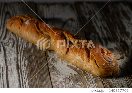 Freshly baked rustic bread loaf resting on an aged wooden table illuminated 140857702