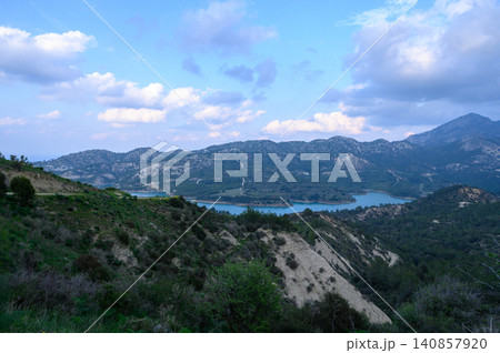 Majestic hills embrace the tranquil lake under a canvas of soft, fluffy clouds at dusk Majestic hills embrace the tranquil lake under a canvas of soft, fluffy clouds at dusk 140857920
