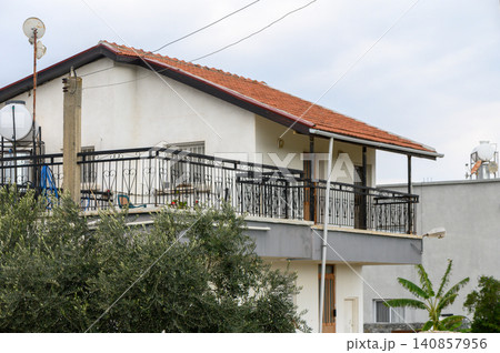 Cozy hillside residence with a red-tiled roof and balcony in a serene neighborhood during cloudy afternoon Cozy hillside residence with a red-tiled roof and balcony in a serene neighborhood during cloudy afternoon 140857956