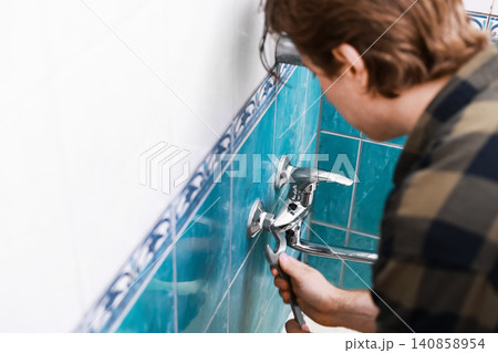 man doing DIY plumbing repairs. This handyman homeowner uses a wrench for a faucet replacement during a bathroom home renovation. man doing DIY plumbing repairs. This handyman homeowner uses a wrench for a faucet replacement during a bathroom home renovation. 140858954