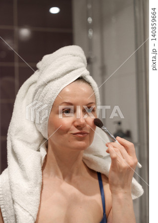 Woman applying make up cosmetic with brush in bathroom Woman applying make up cosmetic with brush in bathroom 140859664