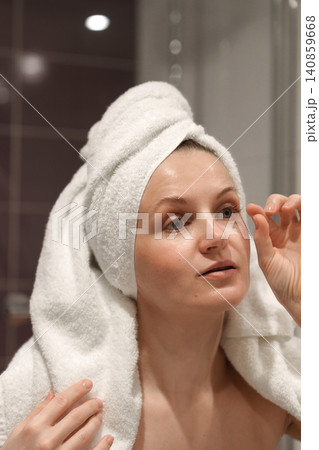 Woman touching up eye makeup in bathroom mirror Woman touching up eye makeup in bathroom mirror 140859668