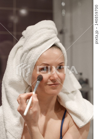 Woman applying make up cosmetic with brush in bathroom Woman applying make up cosmetic with brush in bathroom 140859700
