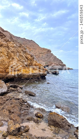Rocky coastal cliff with calm sea under cloudy sky Rocky coastal cliff with calm sea under cloudy sky 140859843