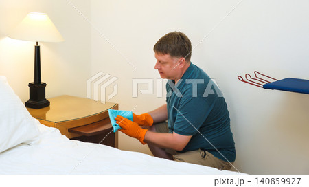 A man of European appearance cleans dust and dirt from a bedside table A man of European appearance cleans dust and dirt from a bedside table 140859927