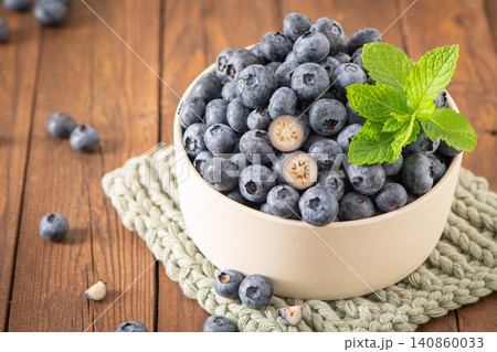 Fresh blueberries in a ceramic bowl with mint leaves on a wooden table, featuring vibrant fruit textures 140860033