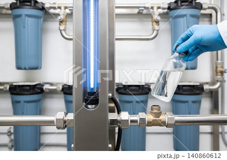 Scientist examines purified water in laboratory filtration system with UV sterilization 140860612