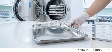 Gloved hand places sterile instrument tray into an open medical autoclave Gloved hand places sterile instrument tray into an open medical autoclave 140860653