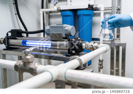 Scientist examines UV water purification system with blue filters and flask 140860728